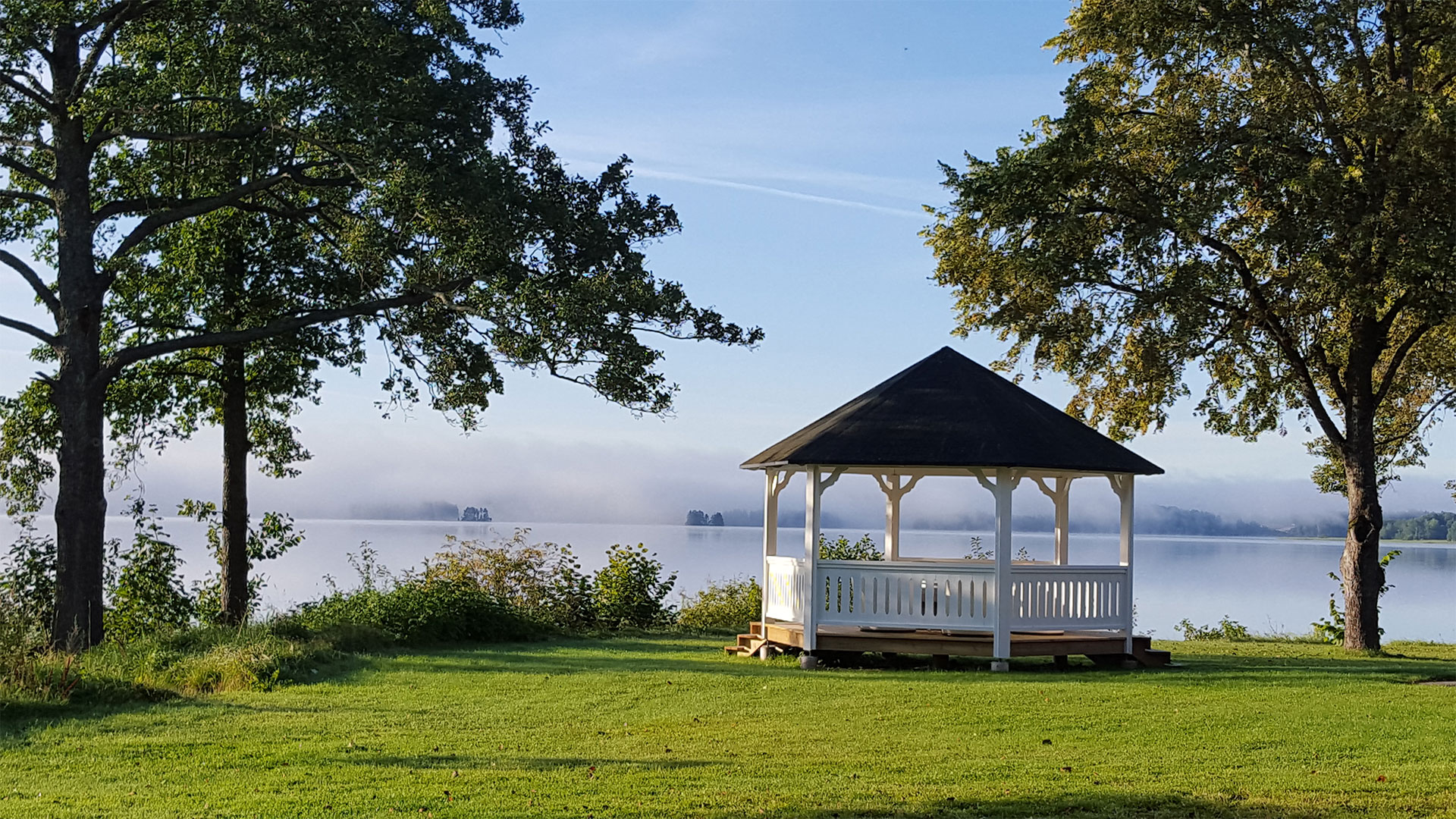 Vit paviljong på gräsmattan vid vattnet